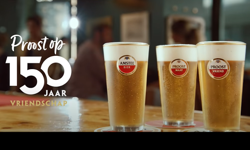 Drie vaasjes Amstel op de bar met de tekst 'Proost op 150 jaar vriendschap' ernaast